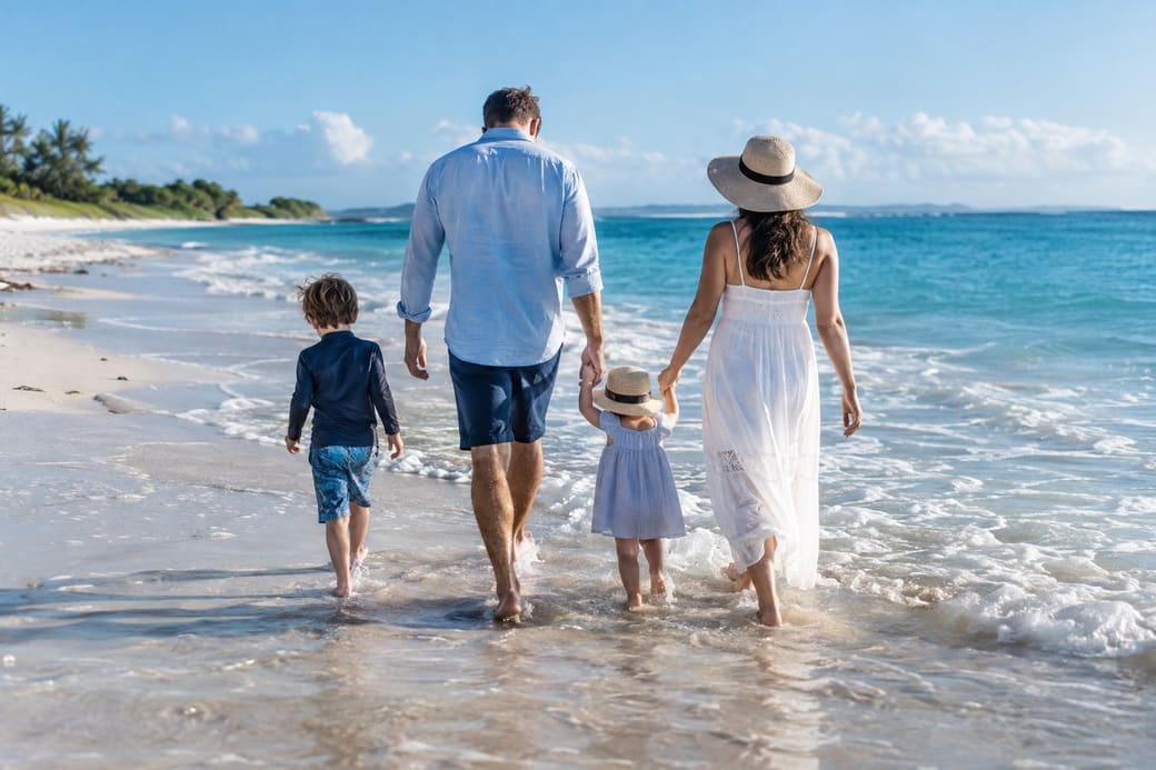 A family walking hand in hand along the water's edge on a sunny beach